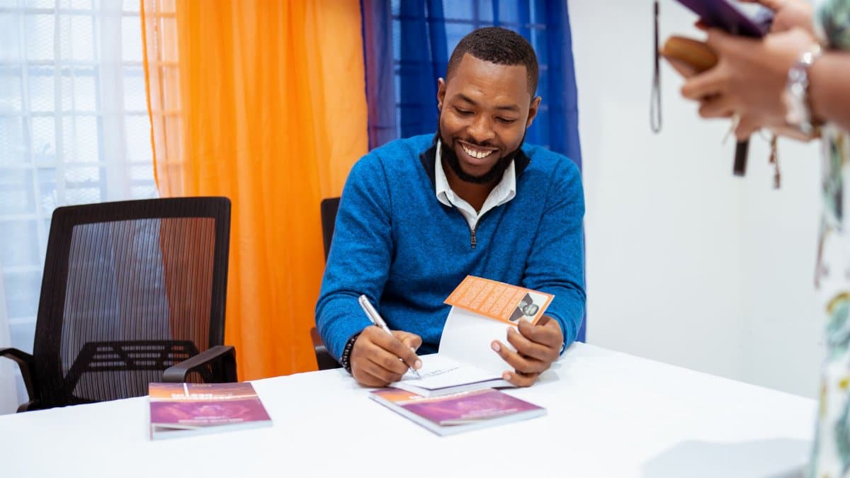 Smiling author signing books at a public event, engaging with readers.