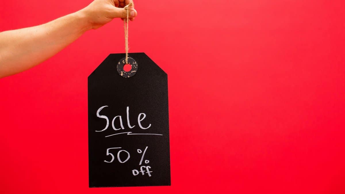 Hand holding a black sale tag with 50% off on a vibrant red background.