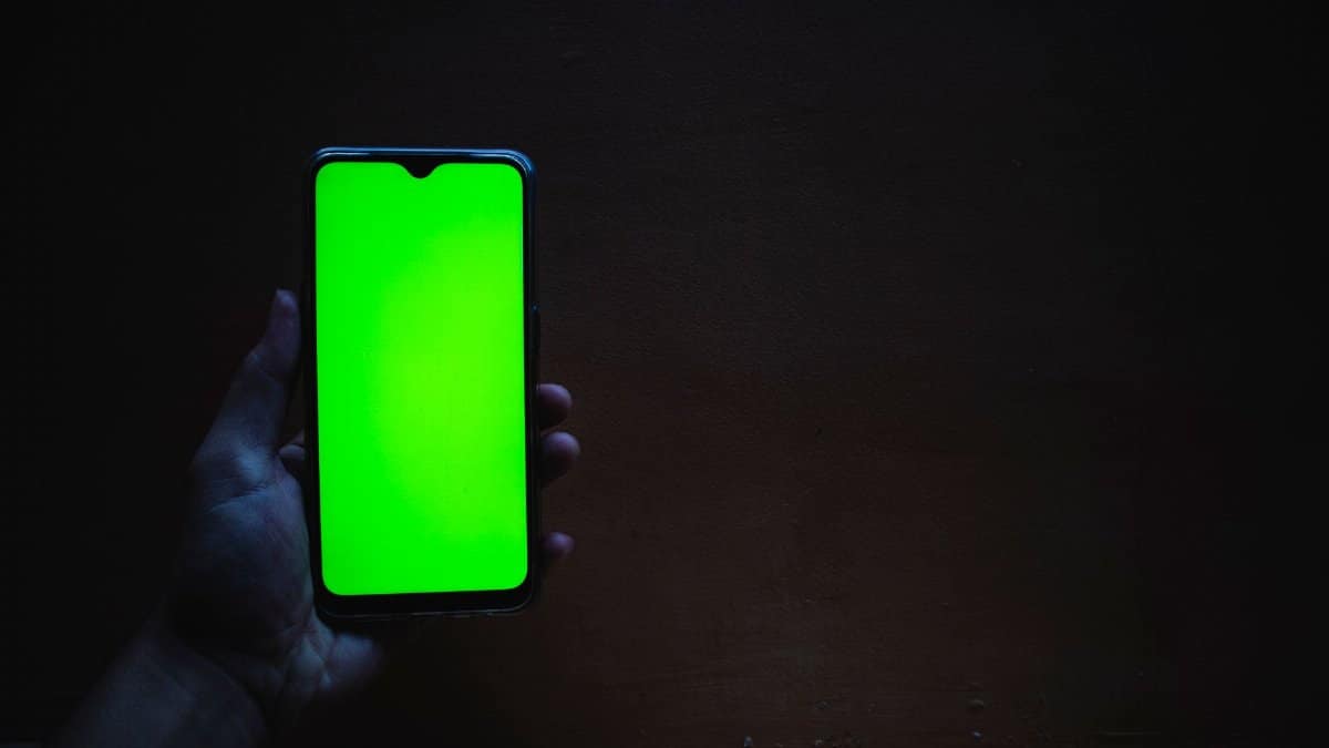 Smartphone with a vivid green screen held against a dark background for mockup use.