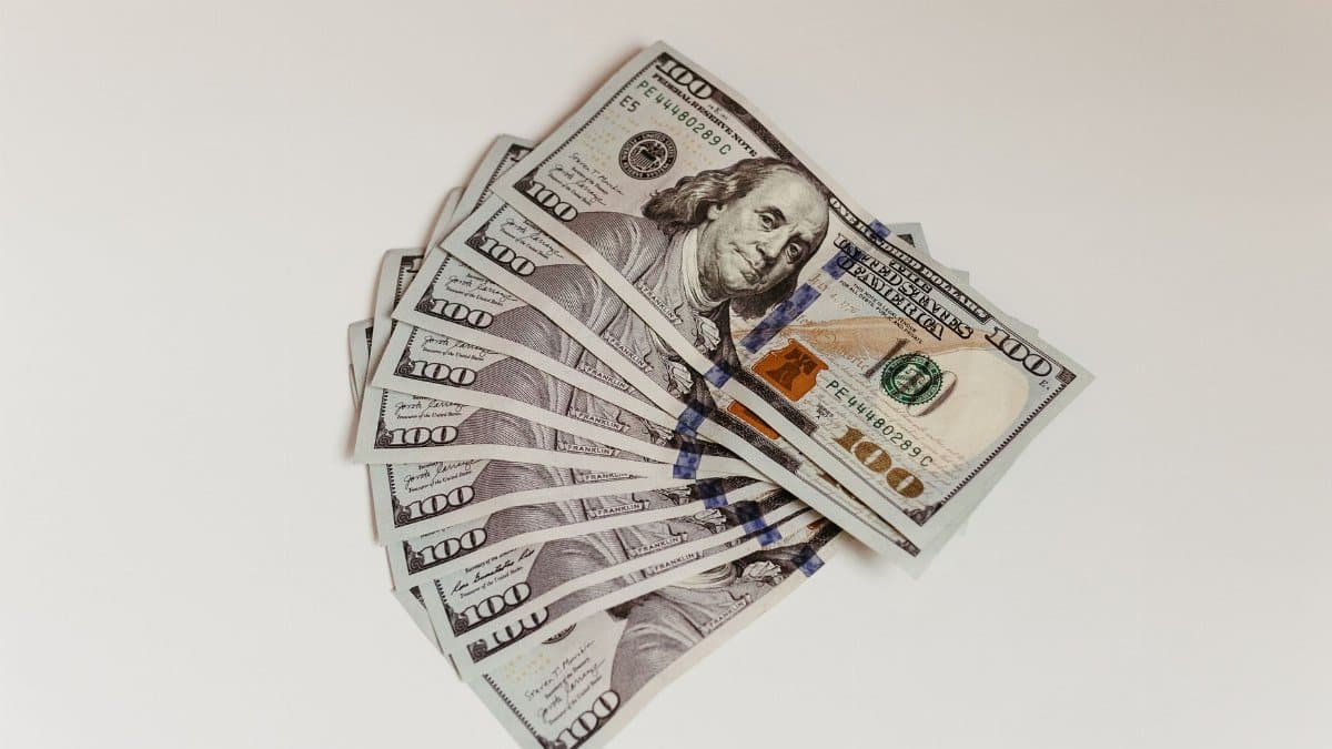Crisp US hundred dollar bills fanned out on a clean white surface, representing wealth and finance.