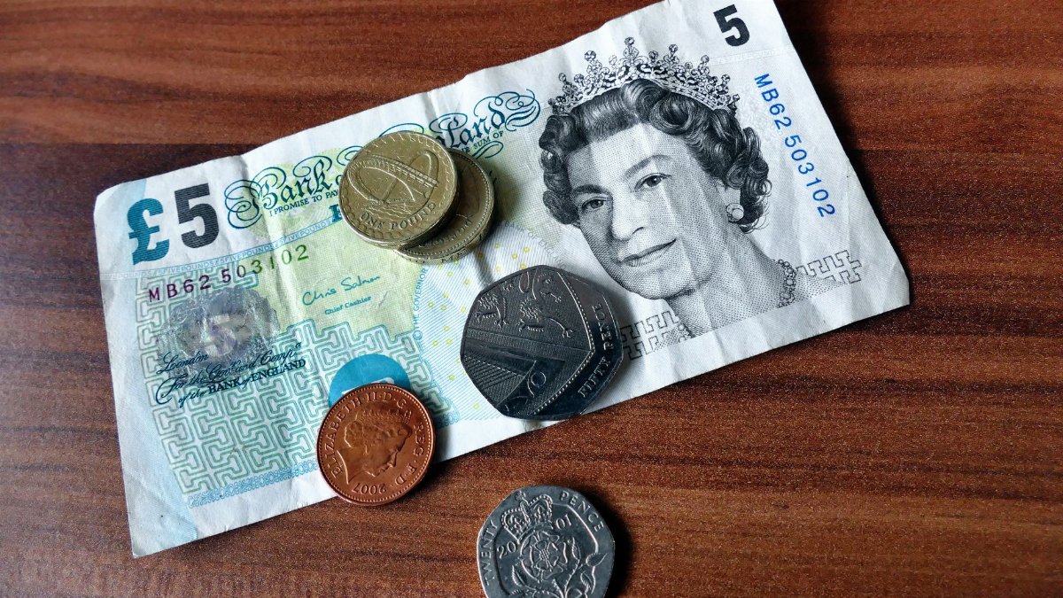 Close-up of a five-pound note and coins representing UK currency on a wooden surface.
