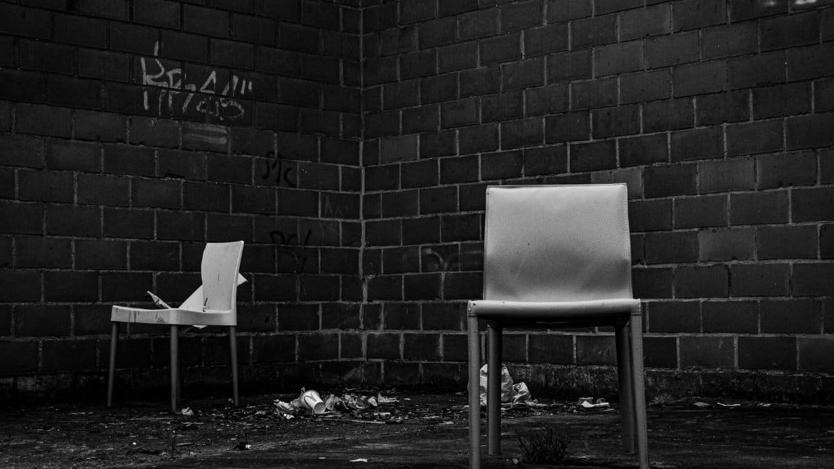 Two empty chairs in a gritty urban environment with graffiti-covered brick walls.
