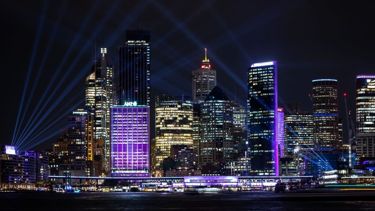 A vibrant night view of Sydney's illuminated skyline with modern architecture and bright city lights.