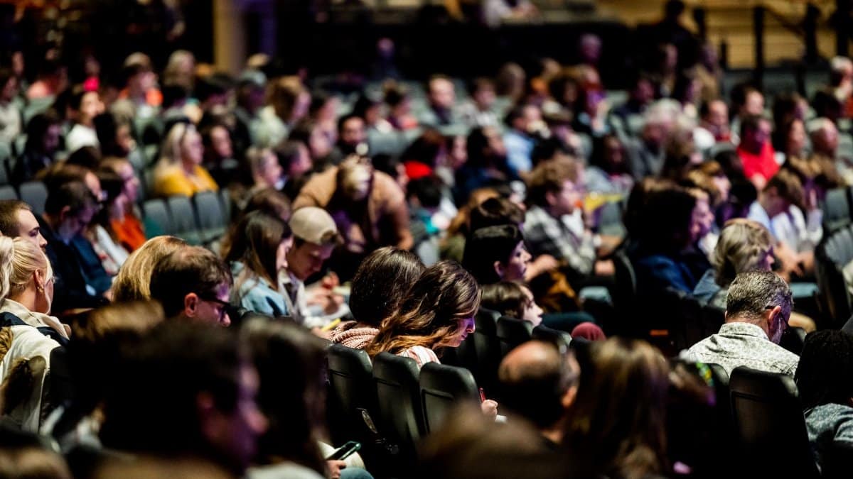 A diverse crowd seated in an auditorium, engaged in an indoor event.