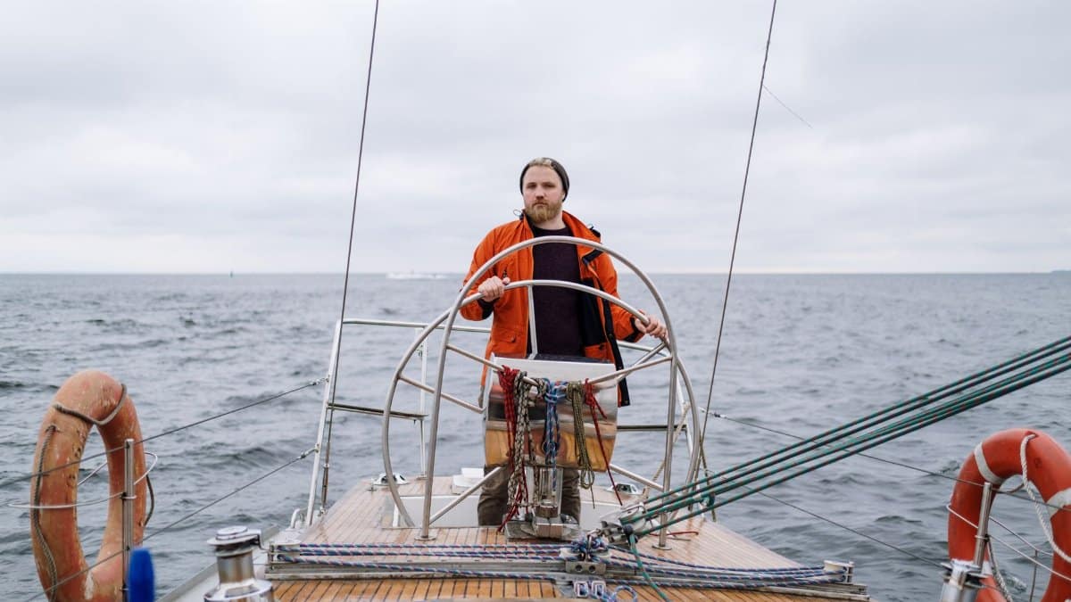 A man confidently steering a sailboat in the vast ocean under a cloudy sky, exploring adventure.