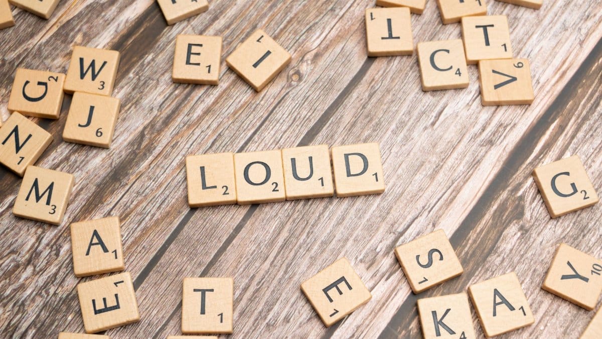 Wooden Scrabble tiles spelling 'LOUD' on a textured wooden background.