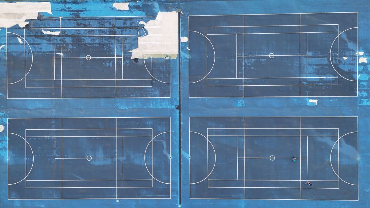 Drone shot of blue multi-sport courts with visible lines and wear from above.