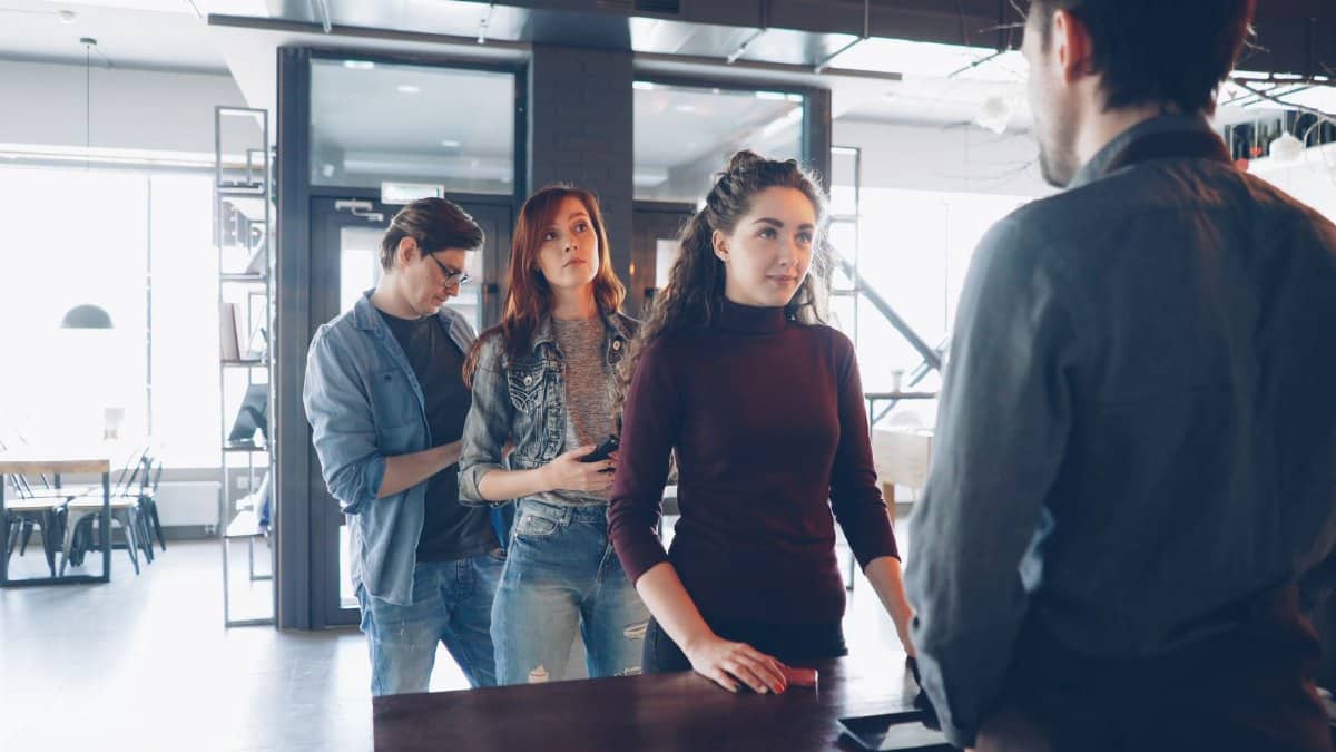 Diverse group of customers waiting in line at a modern cafe with natural lighting.