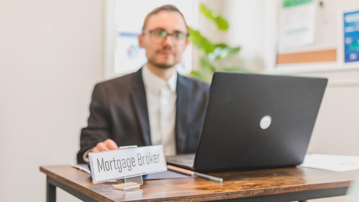 A mortgage broker working at a desk with a laptop in an office setting.