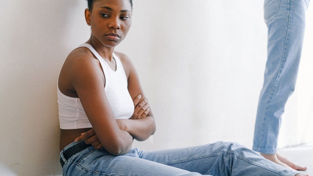 A woman sitting on the floor with crossed arms, expressing deep thought or disagreement.