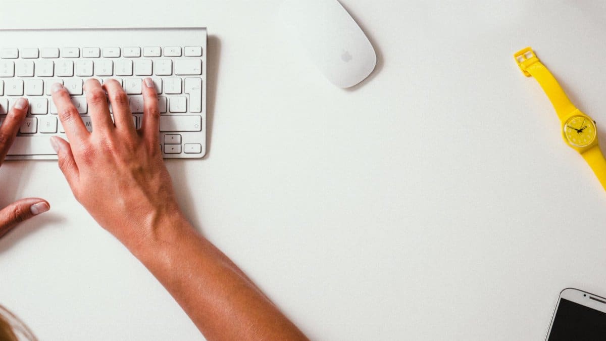 Close-up of hands typing on a keyboard with a yellow watch on the desk