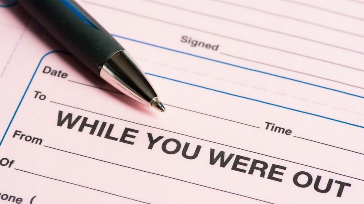 Close-up of a pen and 'While You Were Out' message pad, emphasizing office communication.