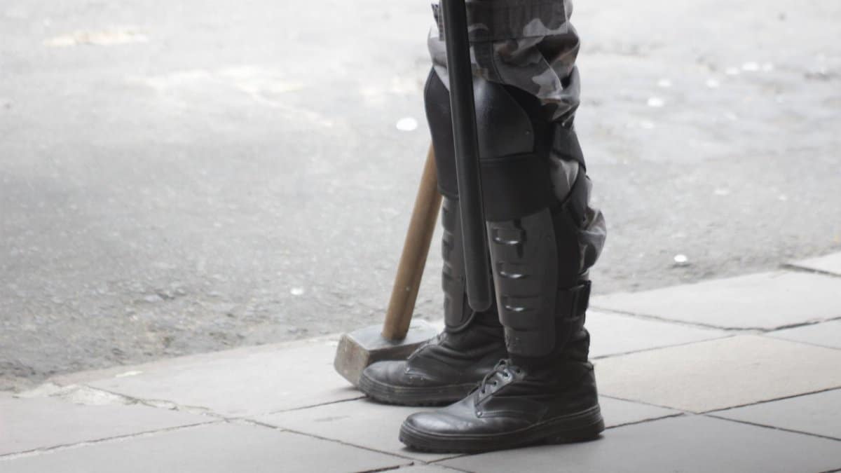 Detailed view of a person standing in protective riot gear and boots on a sidewalk.