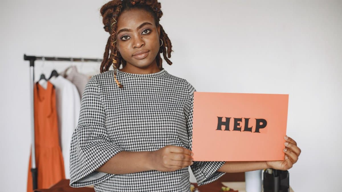 Businesswoman holding a HELP sign, expressing need for assistance or support in a workspace.
