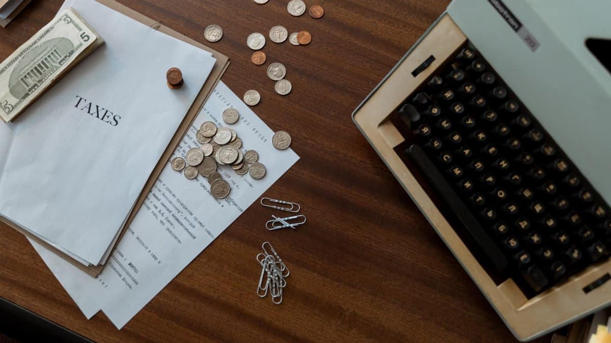 Overhead view of a vintage desk with typewriter, coins, and tax documents.