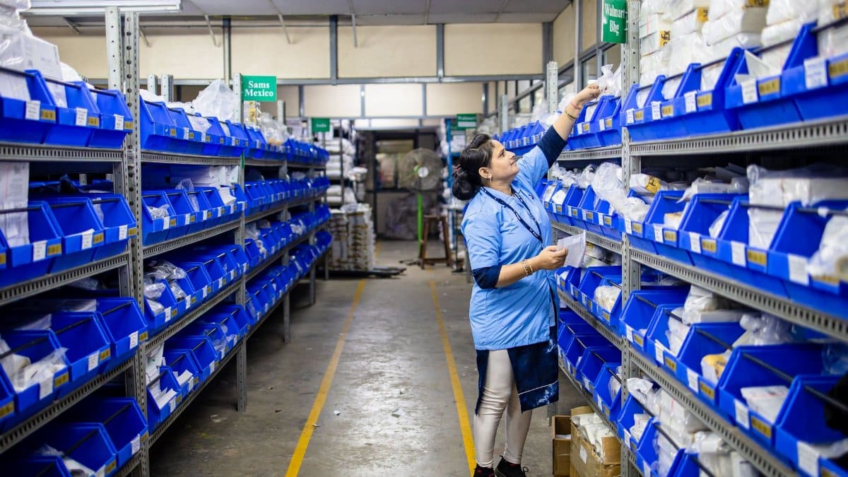 Woman in uniform organizing inventory in a warehouse aisle with labeled bins.