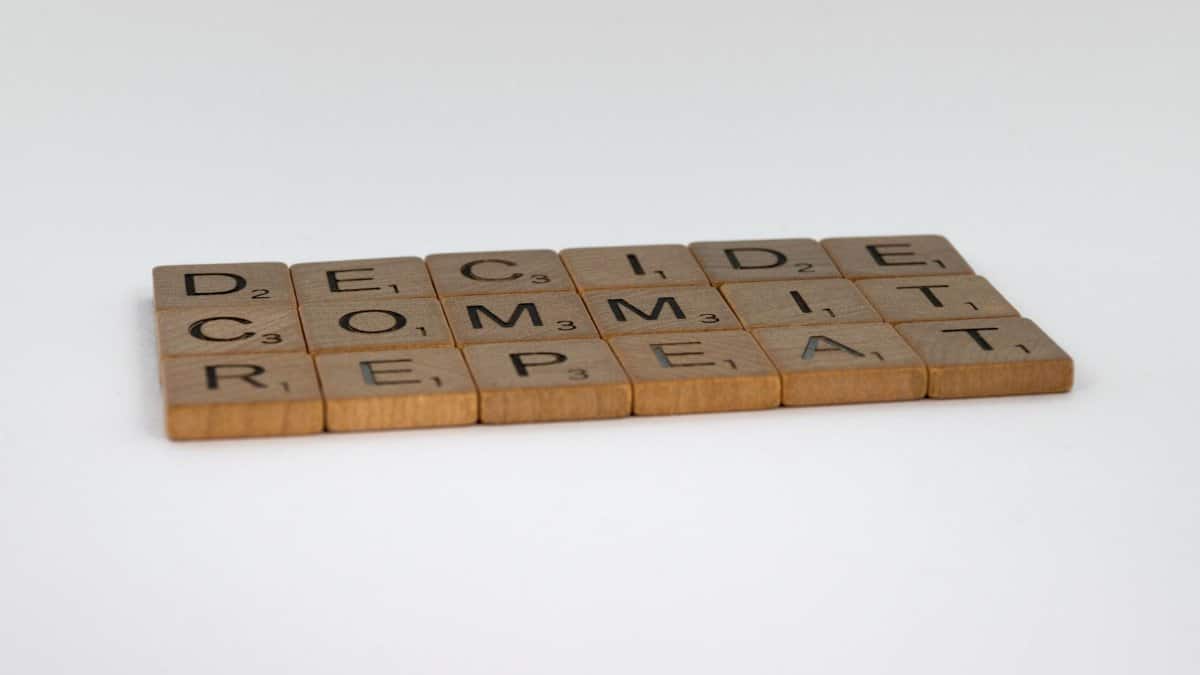 Wooden tiles arranged to spell 'DECIDE COMMIT REPEAT' on a white background.