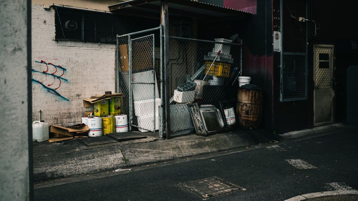 A gritty urban alleyway featuring industrial waste, graffiti, and dim lighting.