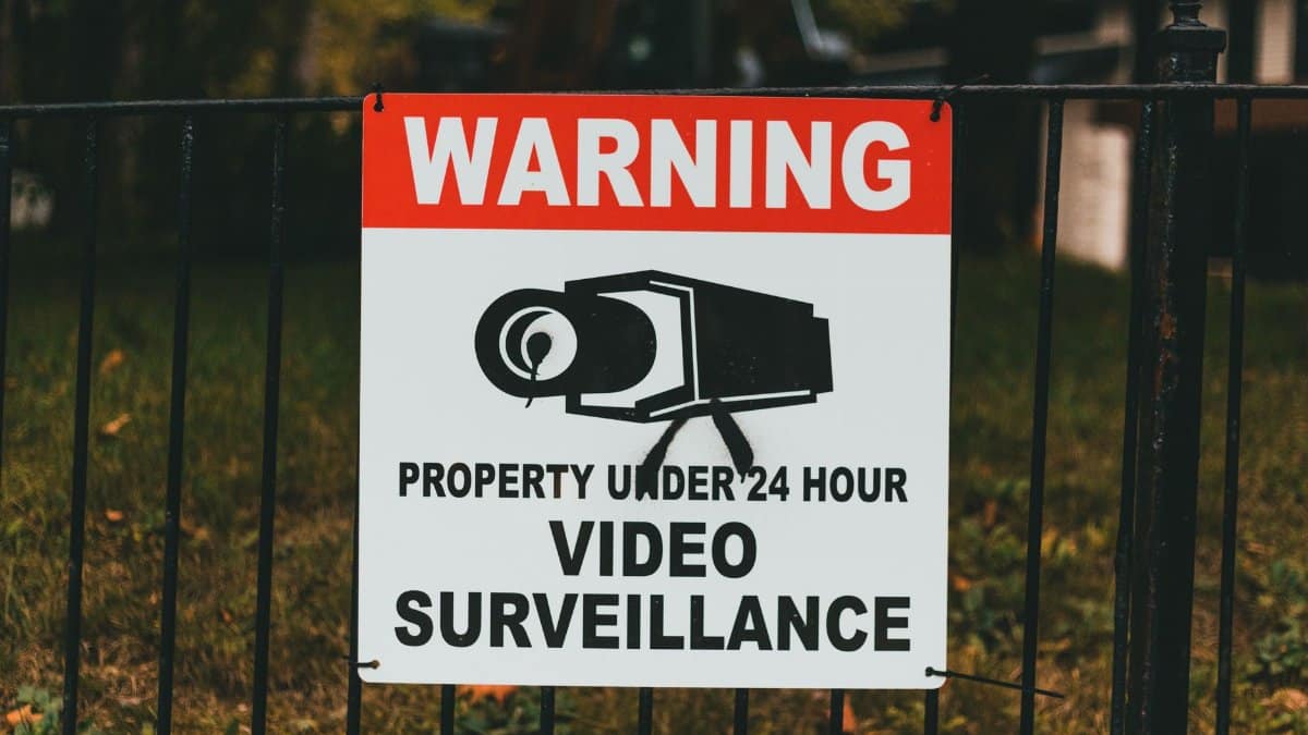 Video surveillance warning sign on metal fence outdoors.