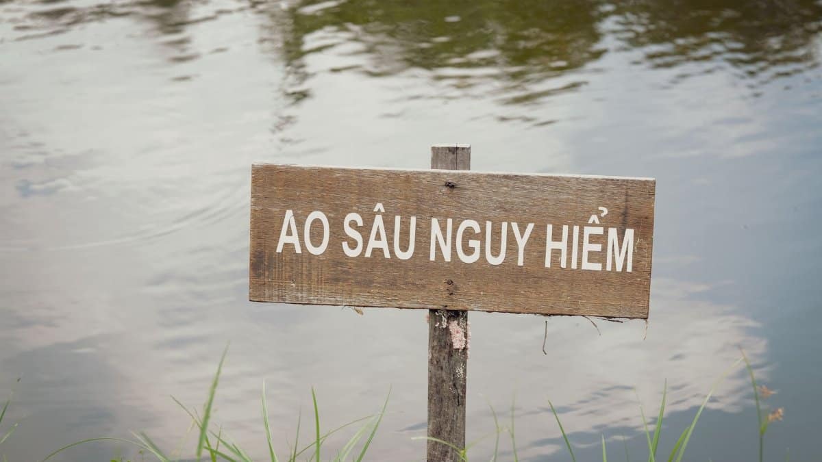 A wooden sign warning of a deep, dangerous pond amidst tranquil outdoor scenery.