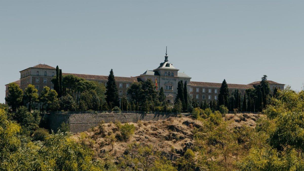 Historic Spanish Military Academy building in Toledo surrounded by trees under clear skies.