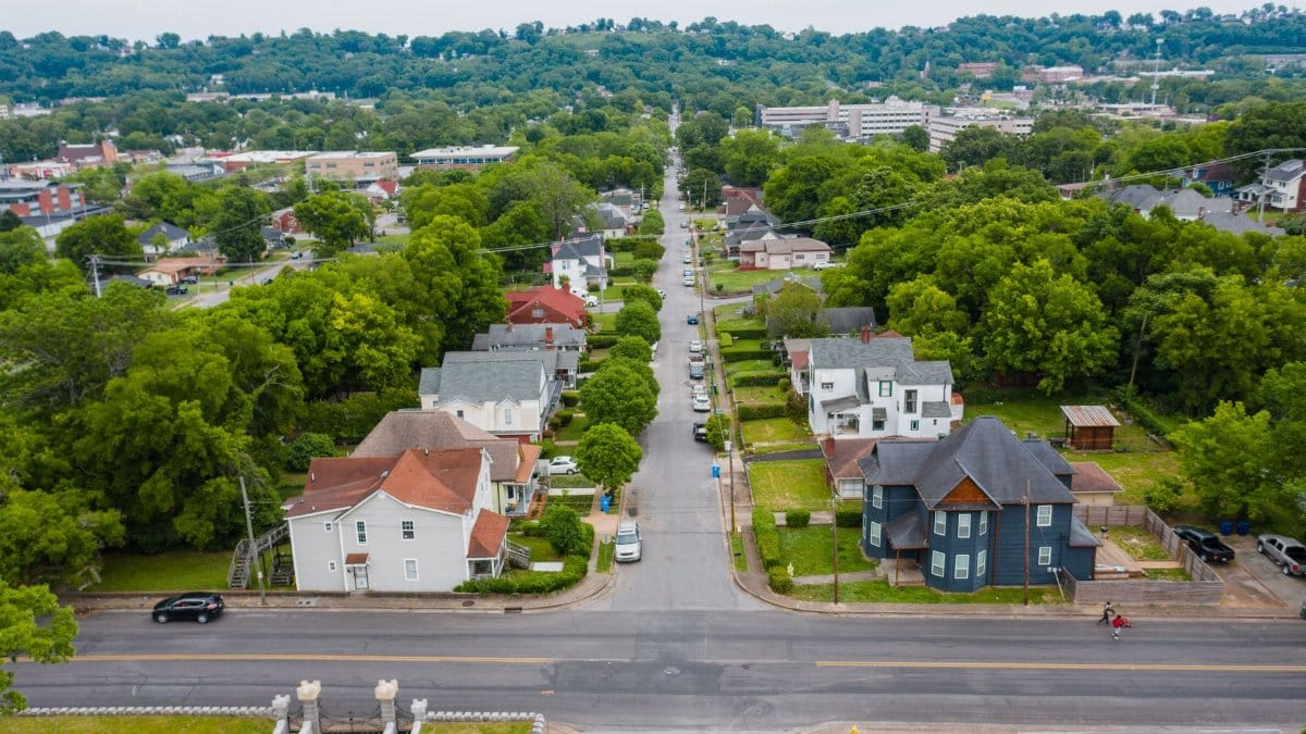 Aerial shot of a green suburban neighborhood with tree-lined streets and residential houses.