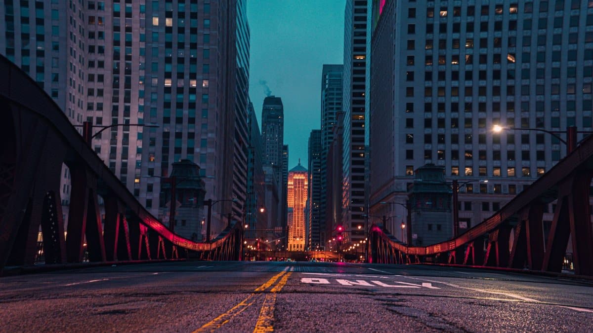 A vibrant cityscape at dusk featuring skyscrapers, a bridge, and illuminated streets.