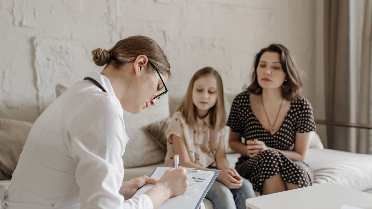 A female doctor consults with a mother and daughter inside a cozy room.