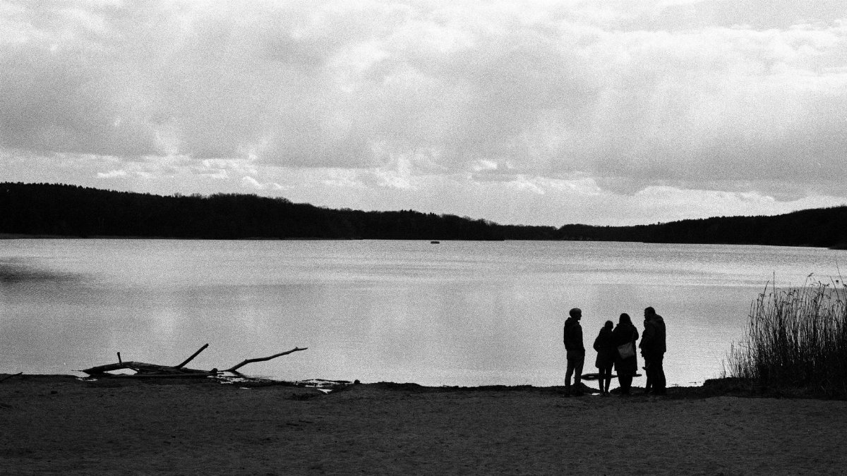 Silhouette of people on a beach by a serene lake in Berlin with a cloudy sky.