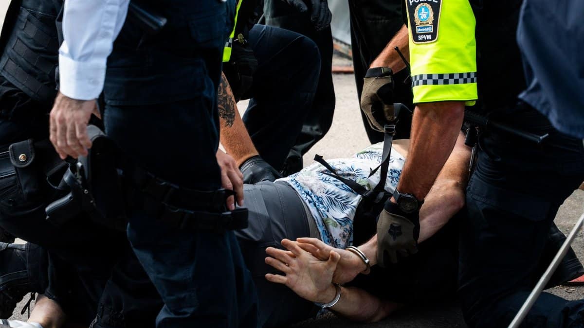 Multiple police officers detain a person on a city street, using handcuffs to restrain them.