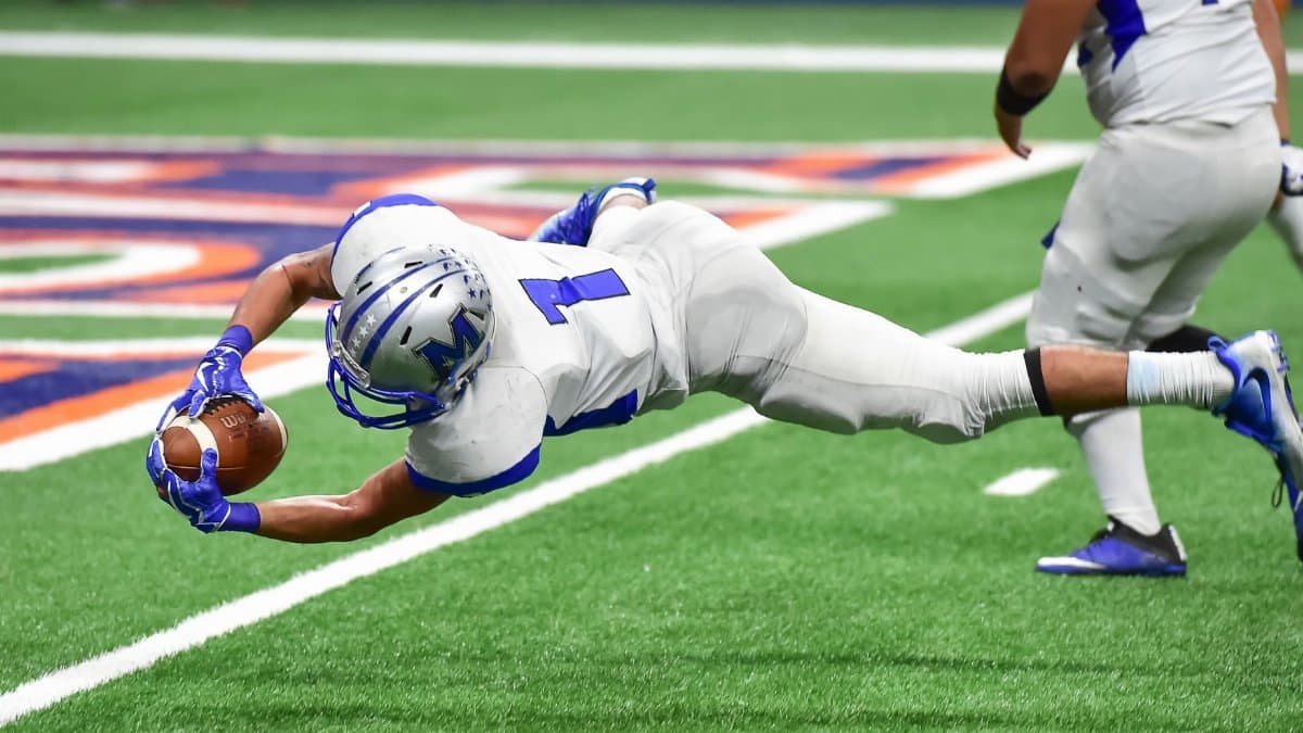 Football player making an incredible diving catch during a high-energy game in the stadium.