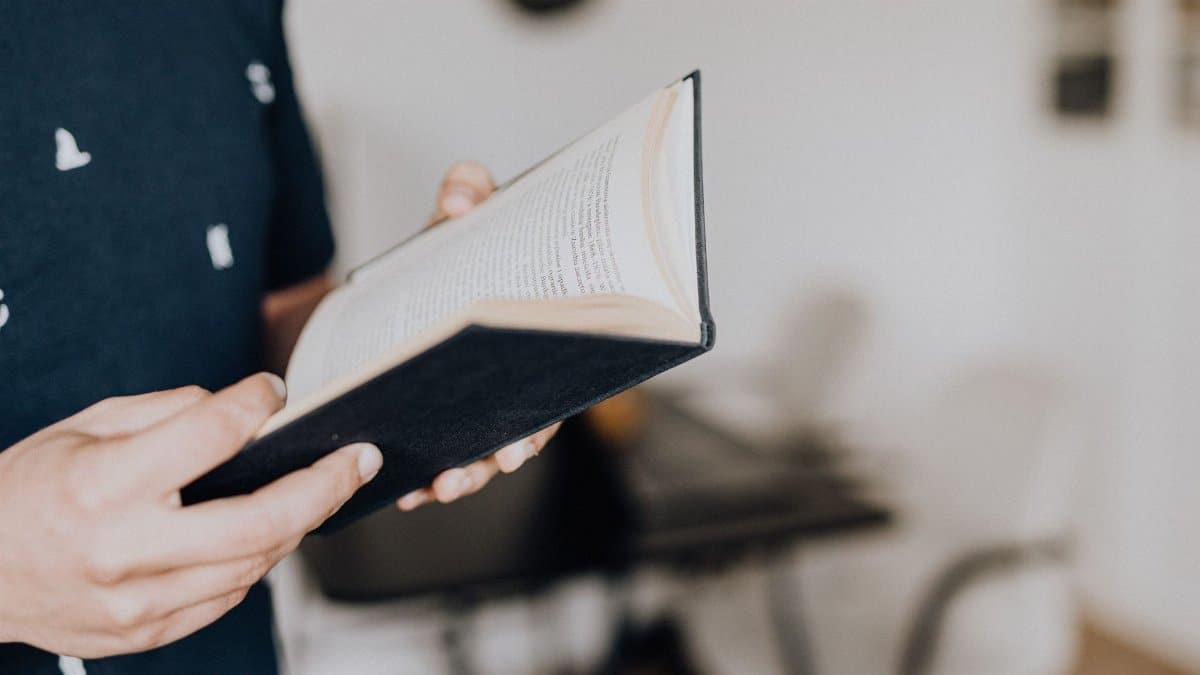 Close-up of hands holding an open book, focused on reading indoors.