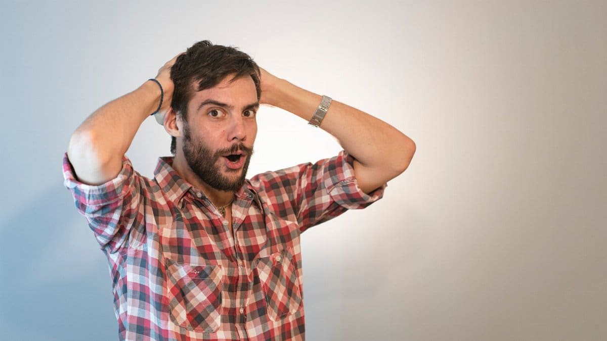 A surprised man with a beard, holding his head in astonishment in a studio setting.