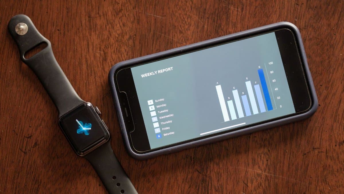 Close-up of a smartphone and smartwatch displaying a weekly report on a wooden table.