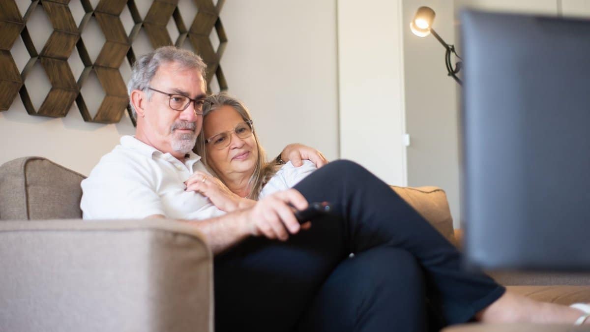 A senior couple enjoys a quiet and happy moment watching television together on the sofa.