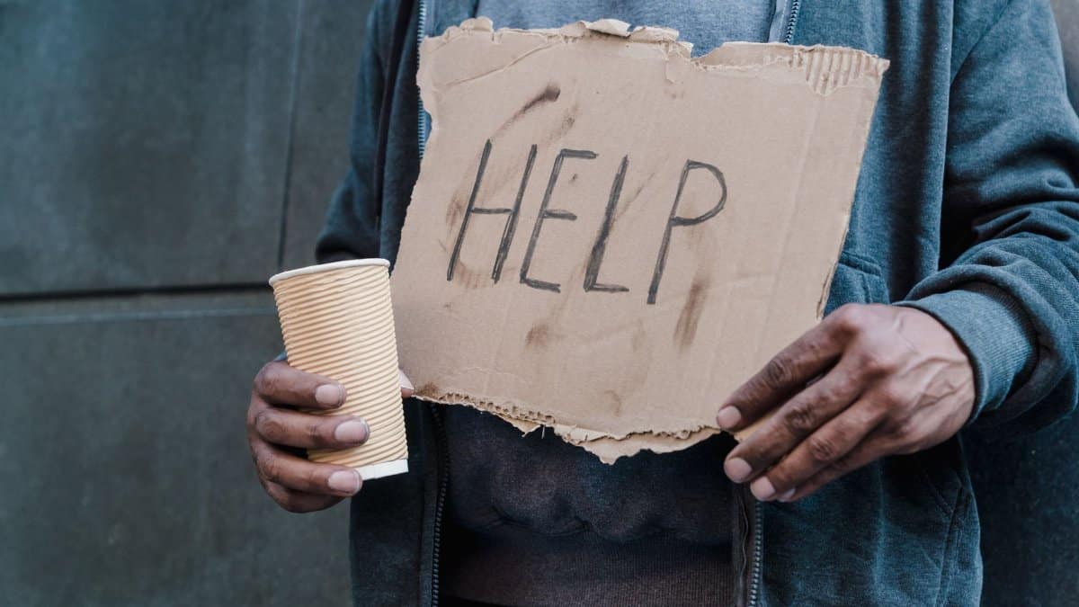 Close-up of a person holding a cardboard sign with 'Help' and a paper cup, representing need and assistance.