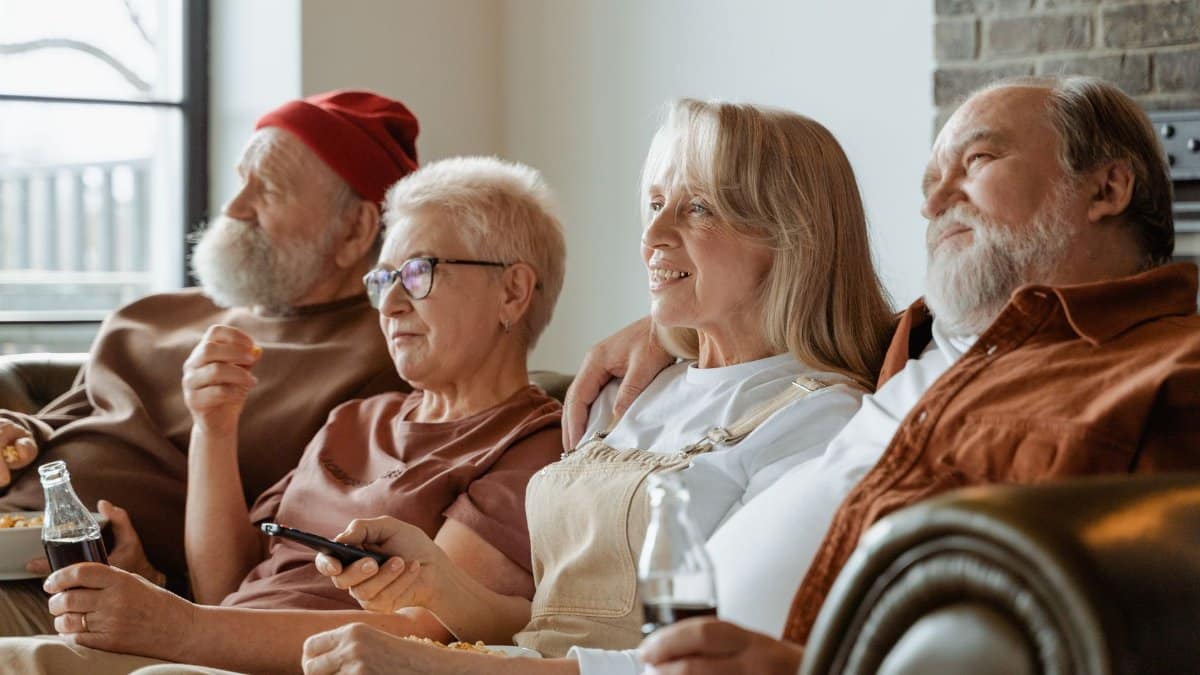 A group of senior adults sharing a cozy moment in a living room, enjoying snacks and drinks.
