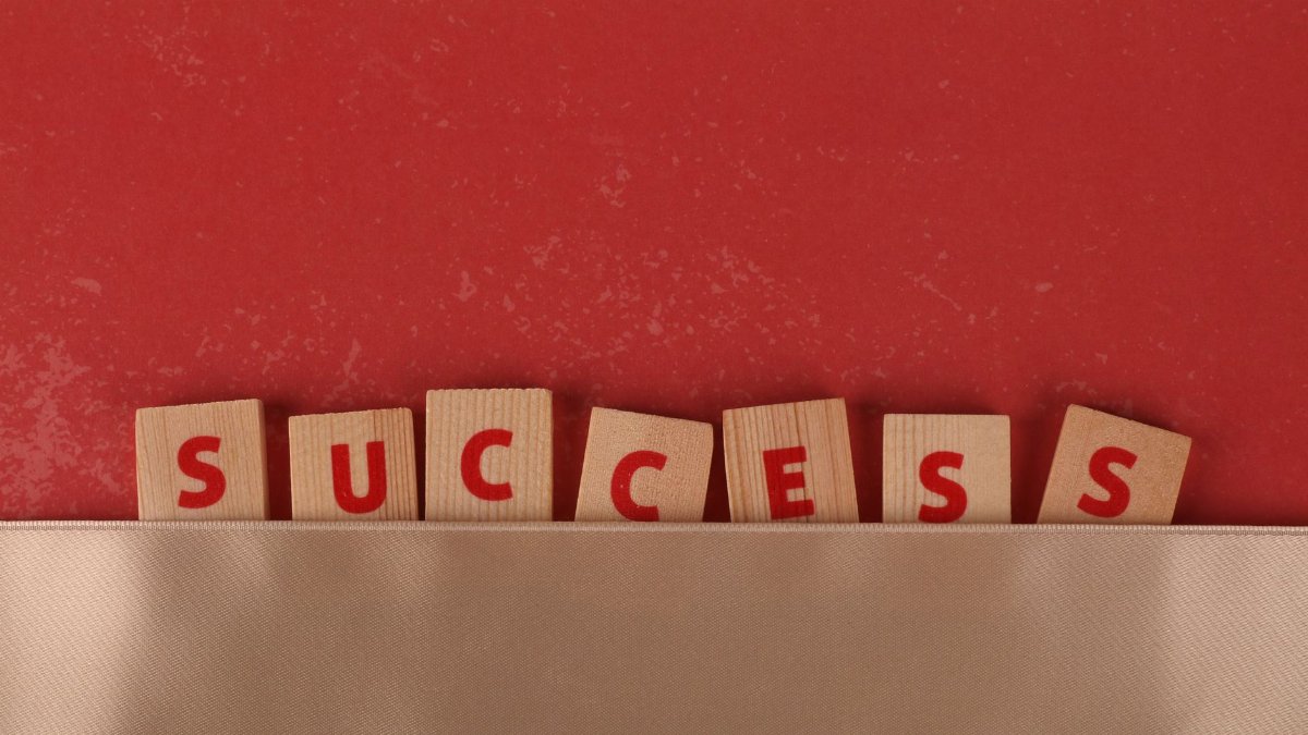 Wooden blocks spelling 'success' on a red background symbolize achievement and growth.