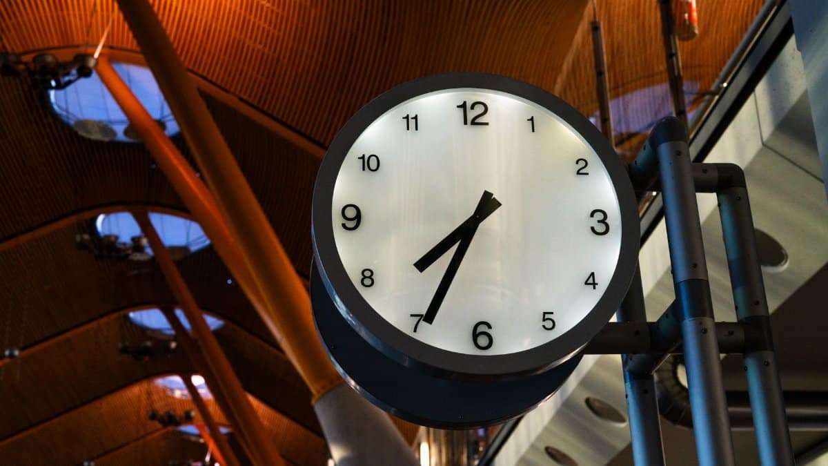 A large clock displaying one o'clock inside a modern airport terminal with a curved ceiling.