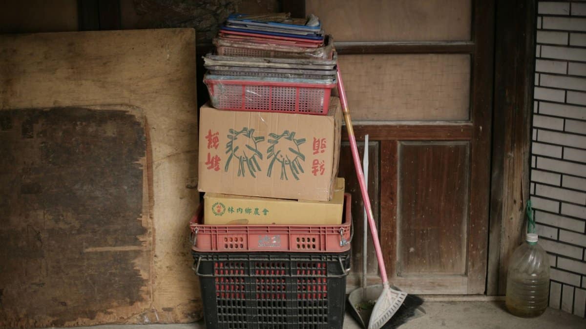 Pile of baskets and cardboard boxes with a mop leaning against a wooden door, creating an urban still life scene.