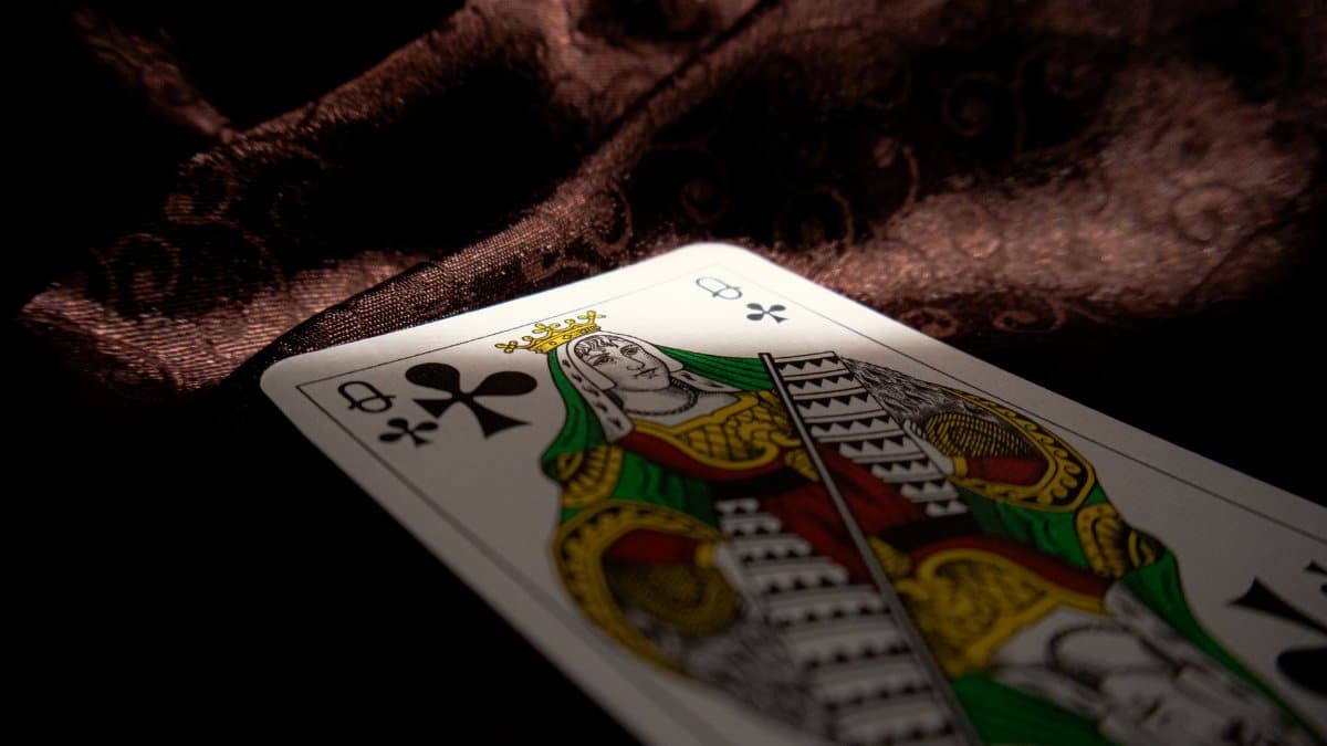 Close-up of a Queen of Clubs playing card on a dark velvet fabric, highlighting themes of gambling and chance.
