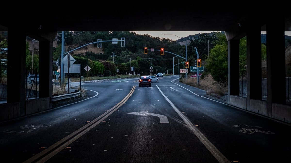 A city intersection under a bridge with cars and traffic lights during dusk.