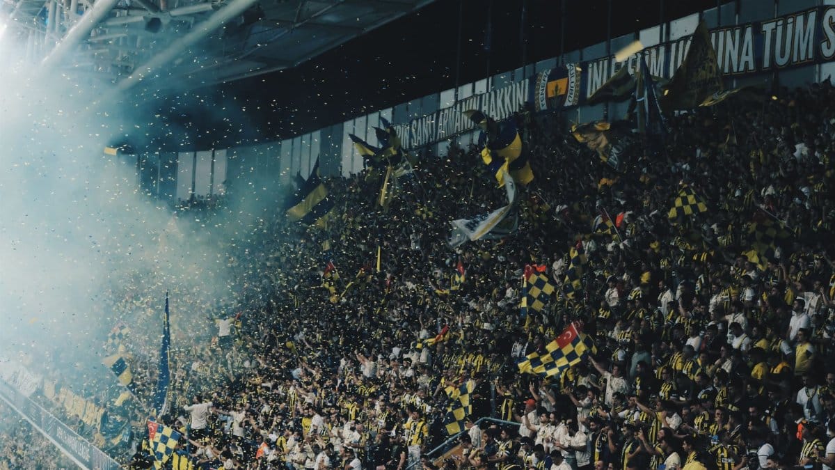 Vibrant crowd cheering with flags and confetti at a lively football match in a stadium.