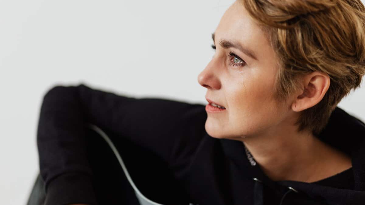 A close-up emotional portrait of a woman shedding a tear, captured indoors.