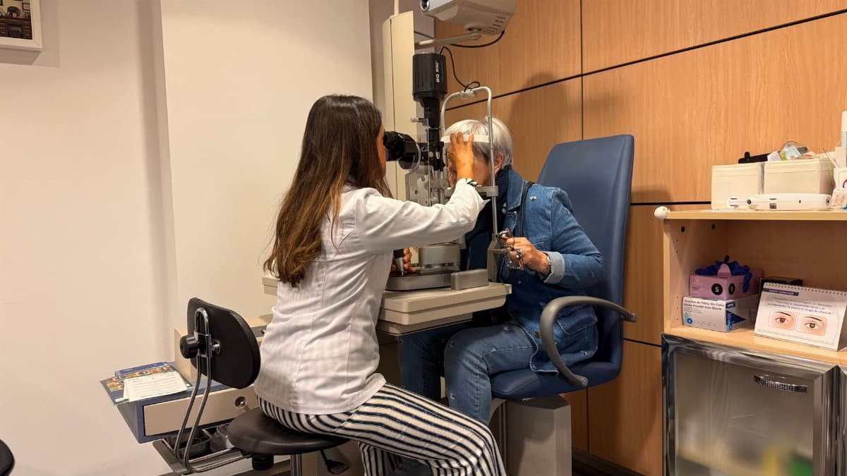 Optometrist performing an eye exam with a slit lamp in a well-lit examination room.