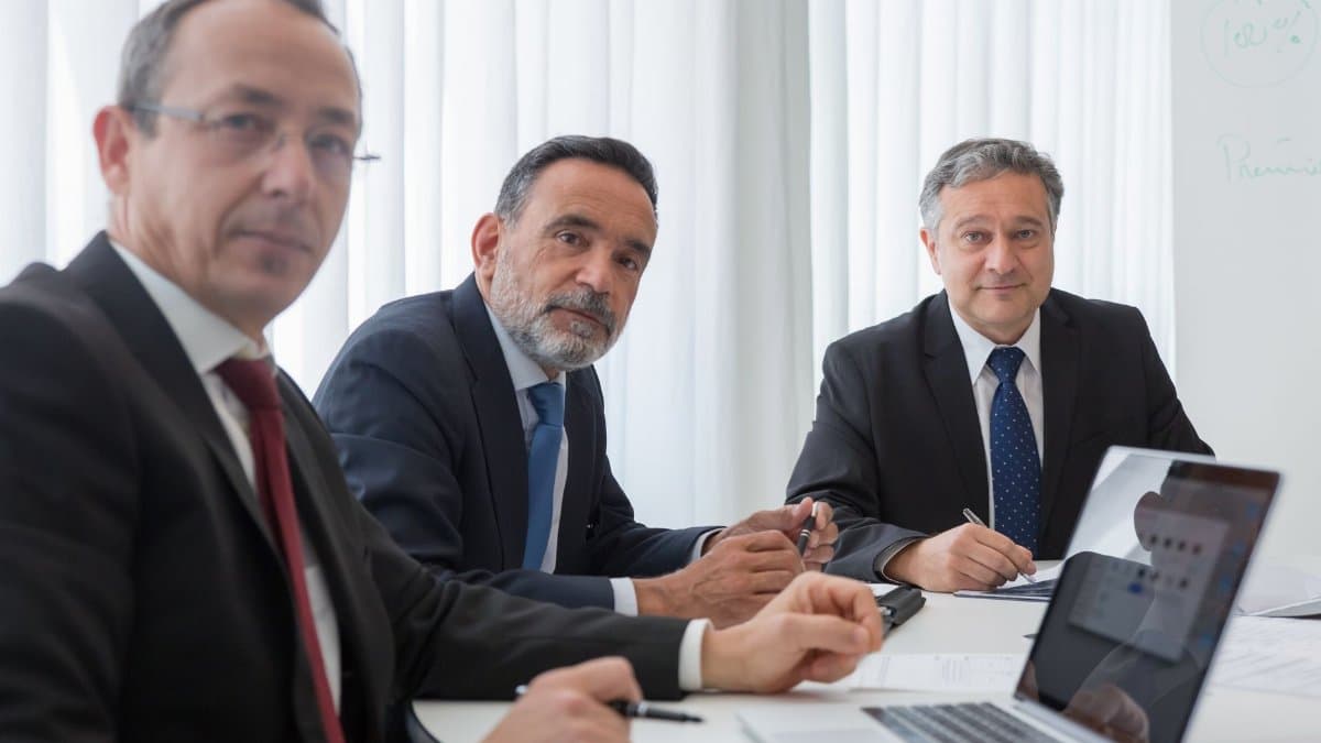 Senior executives in suits conducting a meeting in an office setting.
