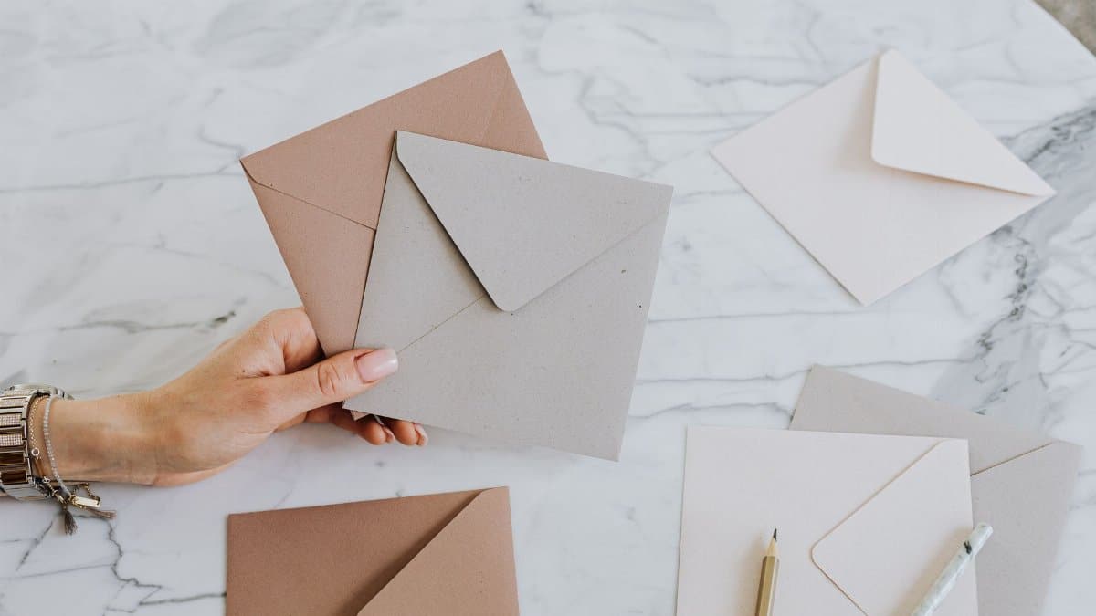 A hand holding craft envelopes on a stylish marble table with pencils, showcasing an artistic layout.