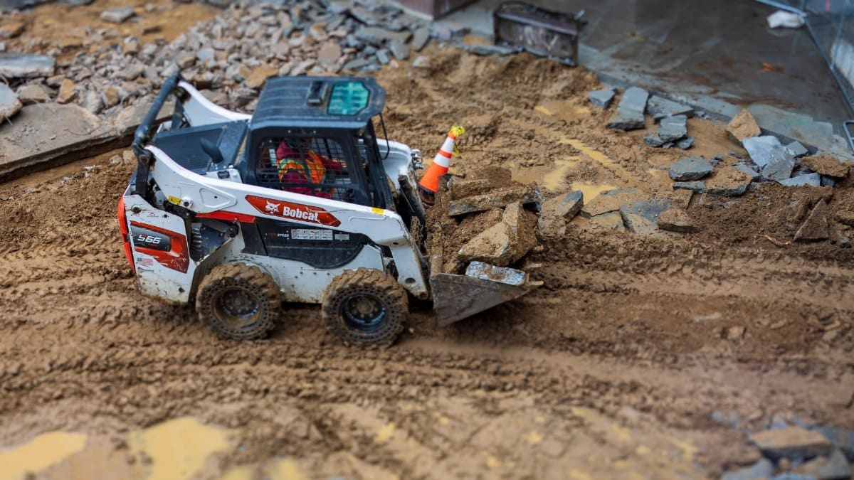 A skid steer loader moves rocks on a muddy construction site, showcasing construction machinery in action.