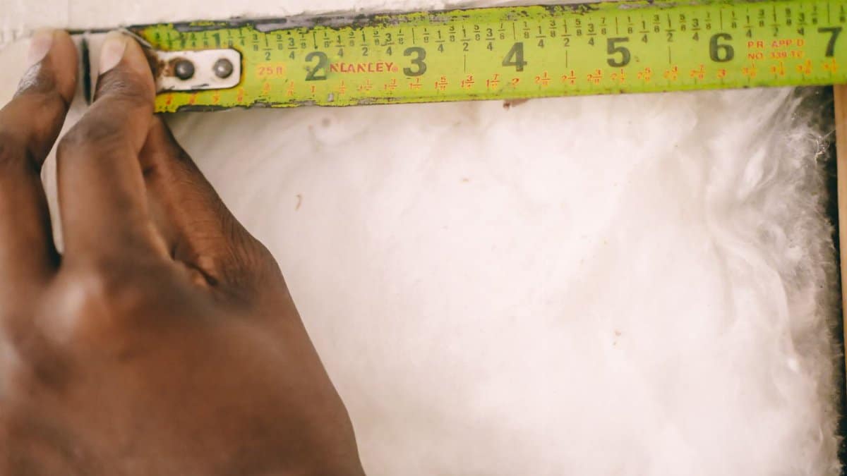 Close-up of a hand measuring insulation with a yellow tape measure.