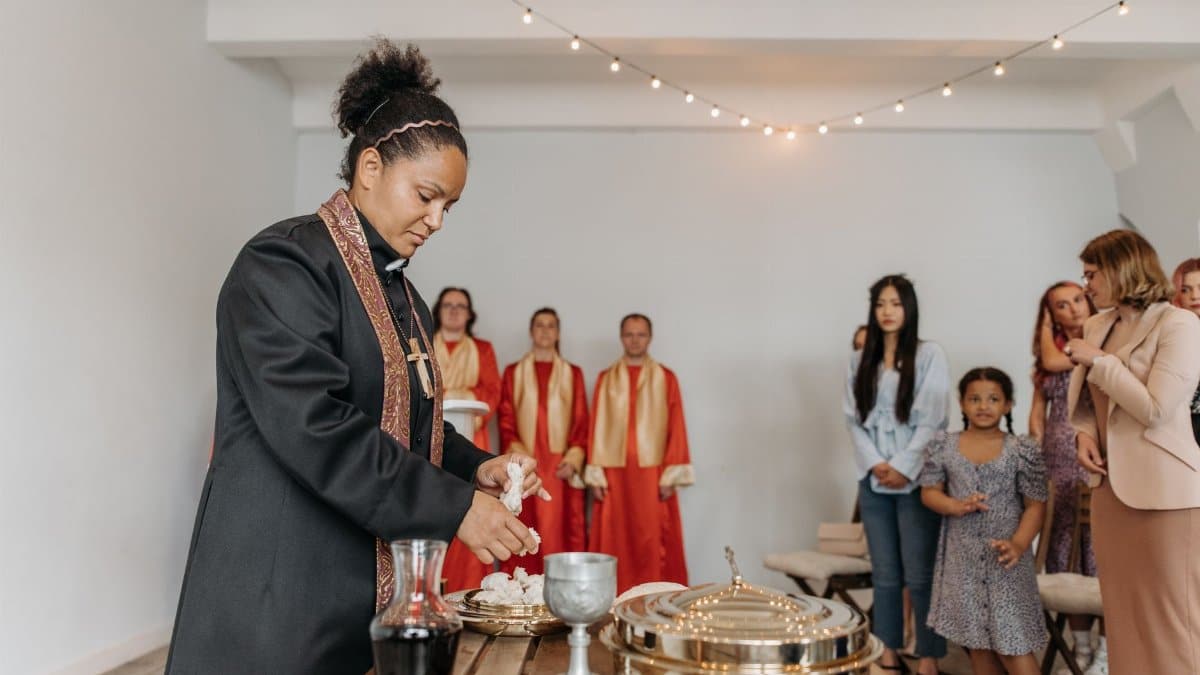 A diverse group of people attending a religious ceremony with a priest performing rituals indoors.